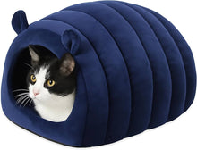 A black and white cat tucked inside the navy velvet hideaway with only its face showing at the entrance